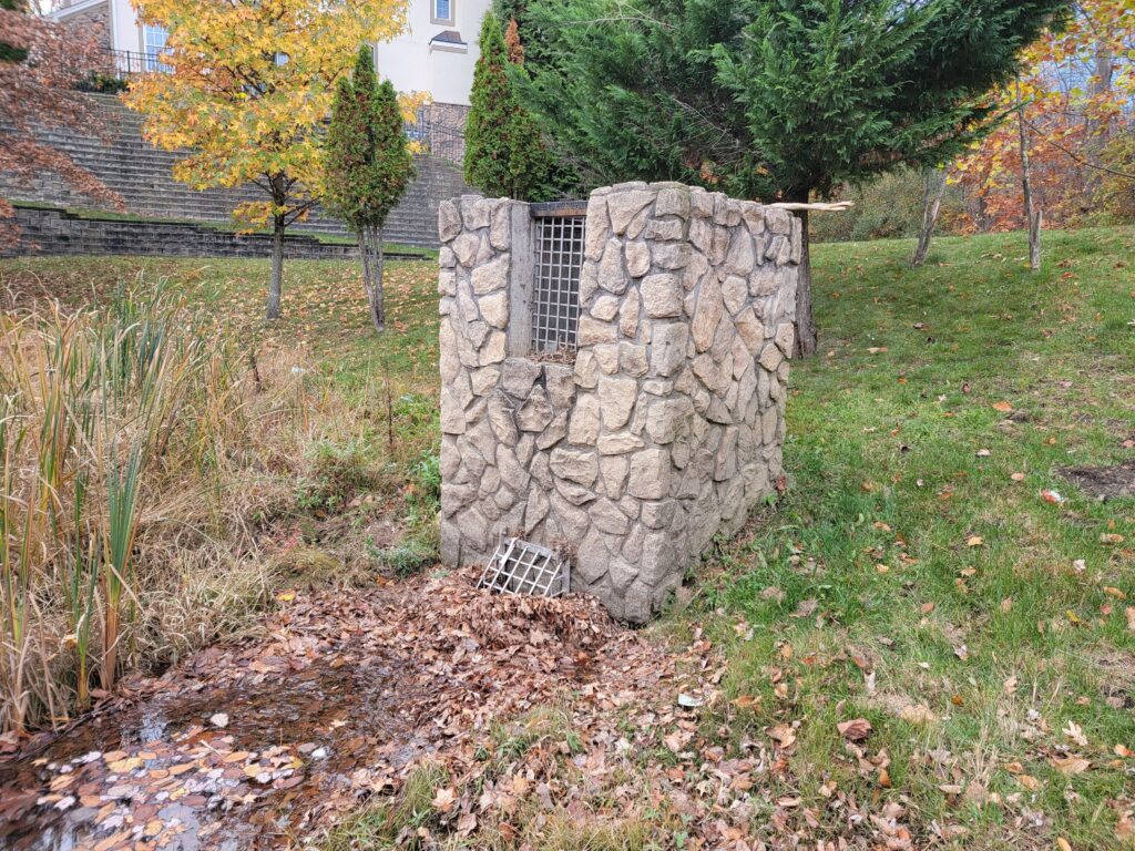 Bubble-up stormwater outlet control structure in a grassy area, designed to manage water discharge and prevent erosion.