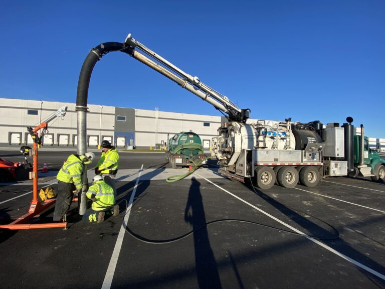 Technicians performing hydrodynamic separator maintenance using a vacuum truck at an industrial site.