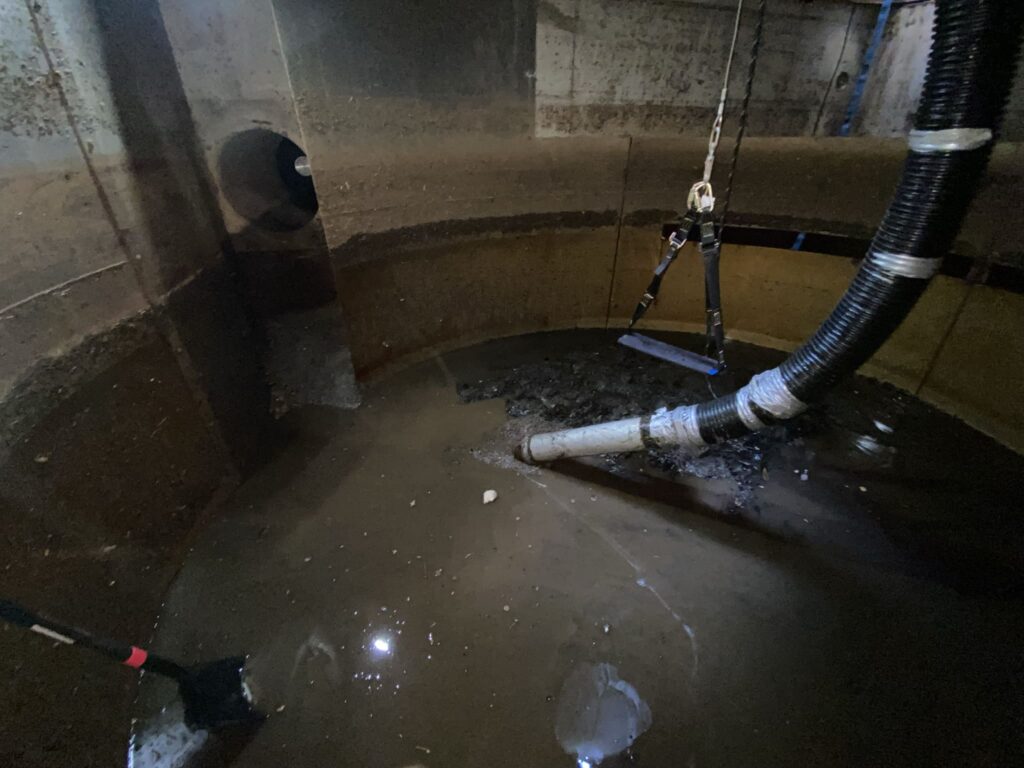 Interior view of a stormwater treatment device during routine maintenance, showing pipes and accumulated sediment.